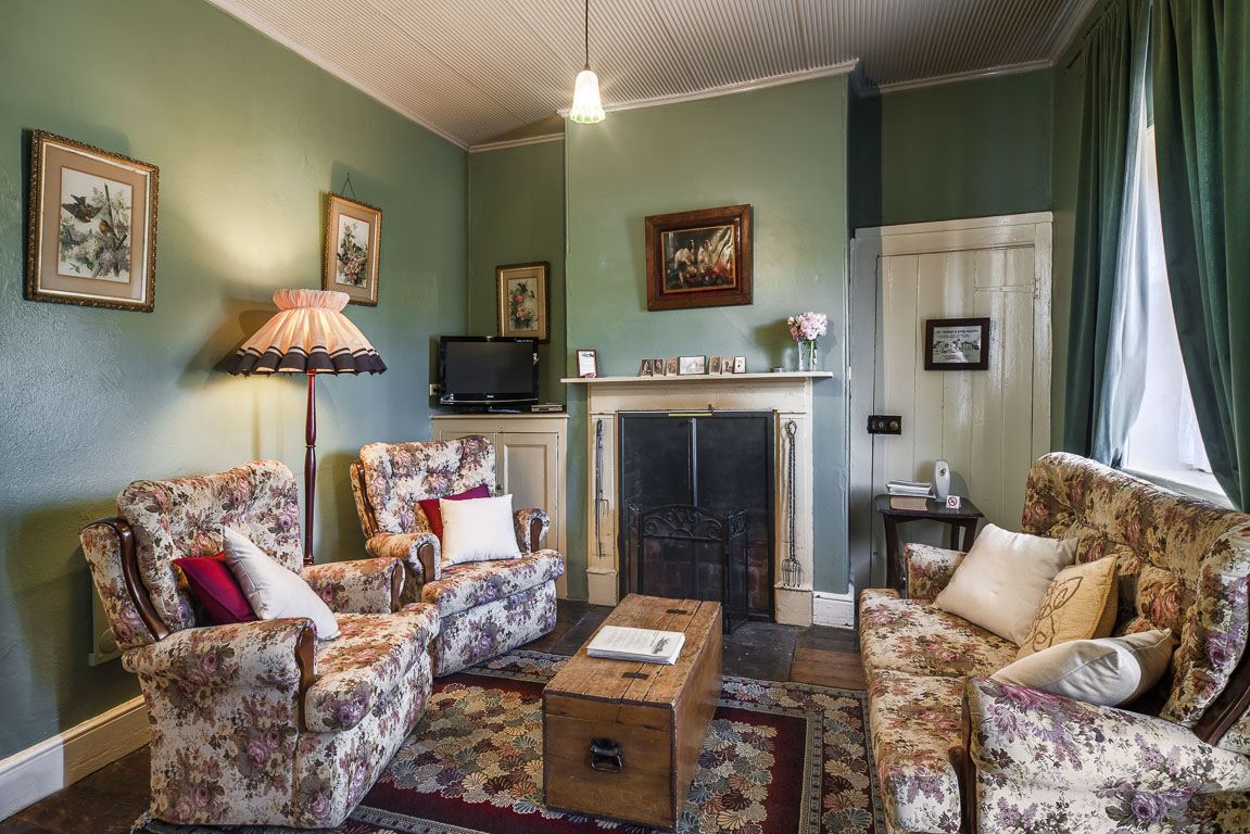 The parlour: floral armchairs around an open fireplace, sage green walls, table lamps lit