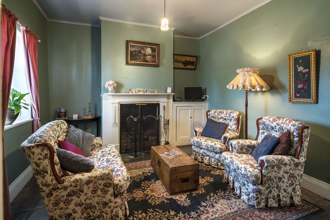 The parlour fireplace with armchairs drawn up close and lamps lit