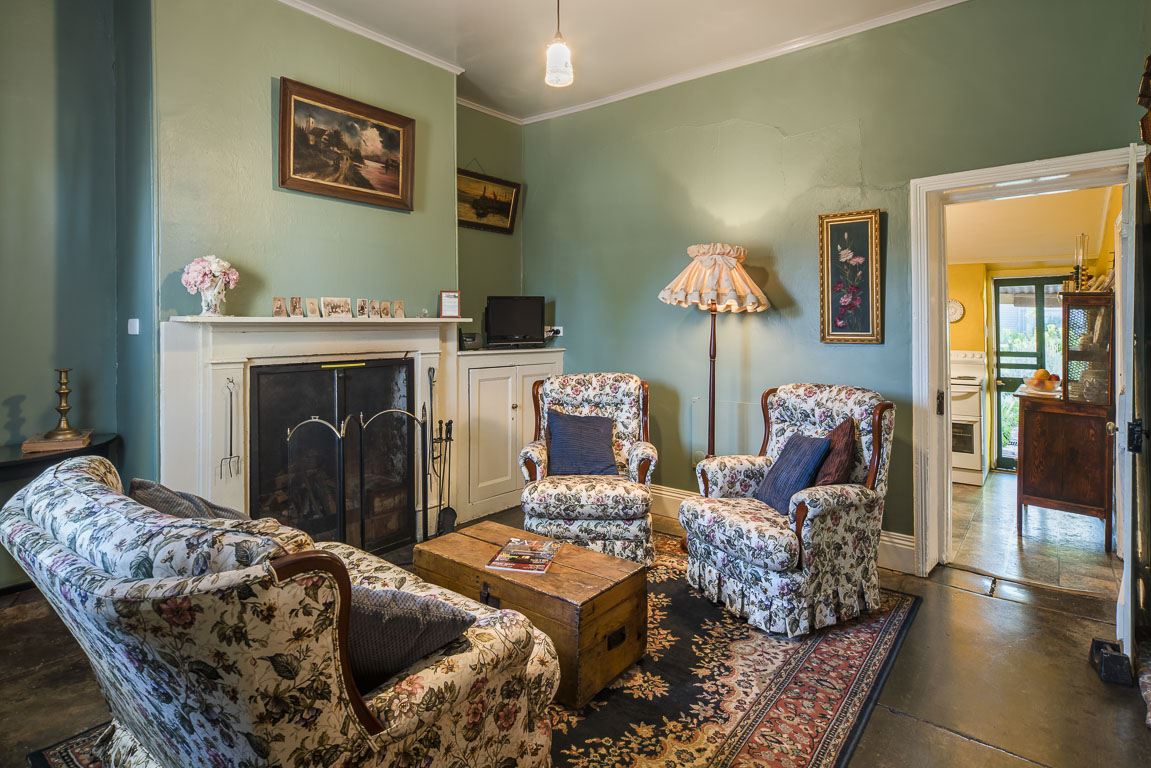 Cottage 10's parlour: armchairs and a sofa around the fireplace, doorway through to the kitchen