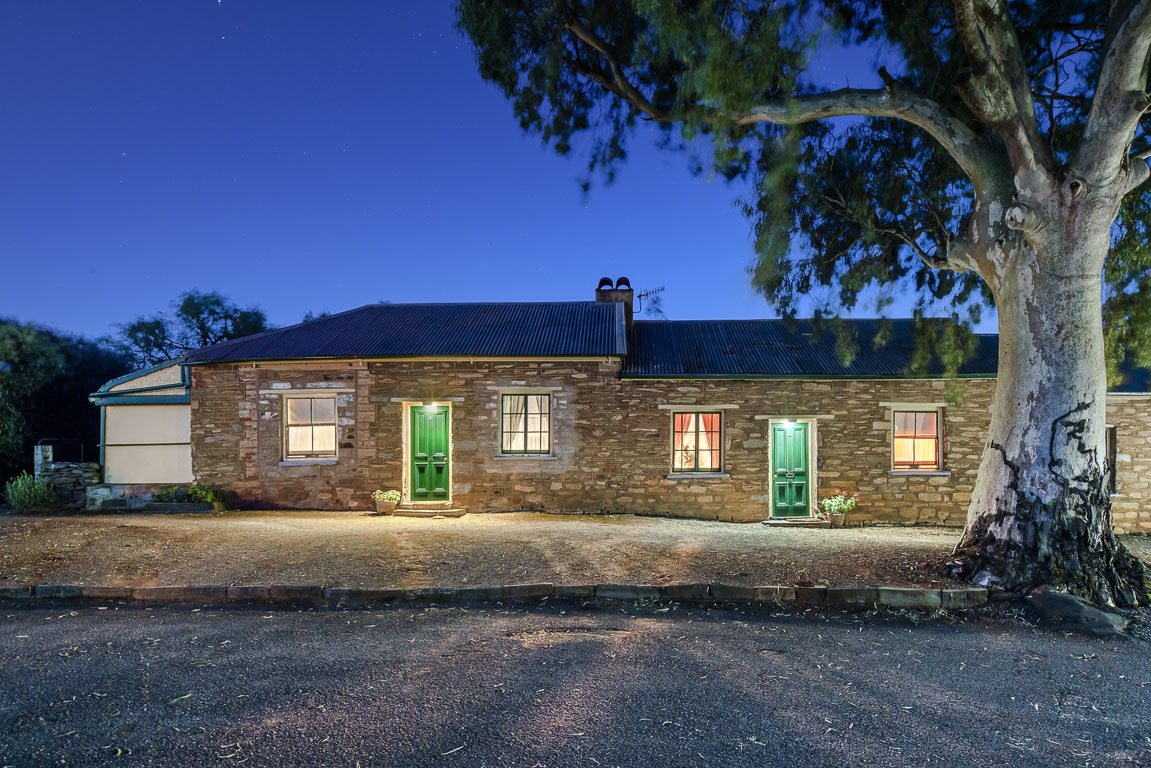 The Tivers Row stone cottages at dusk, windows lit, beneath a large river gum